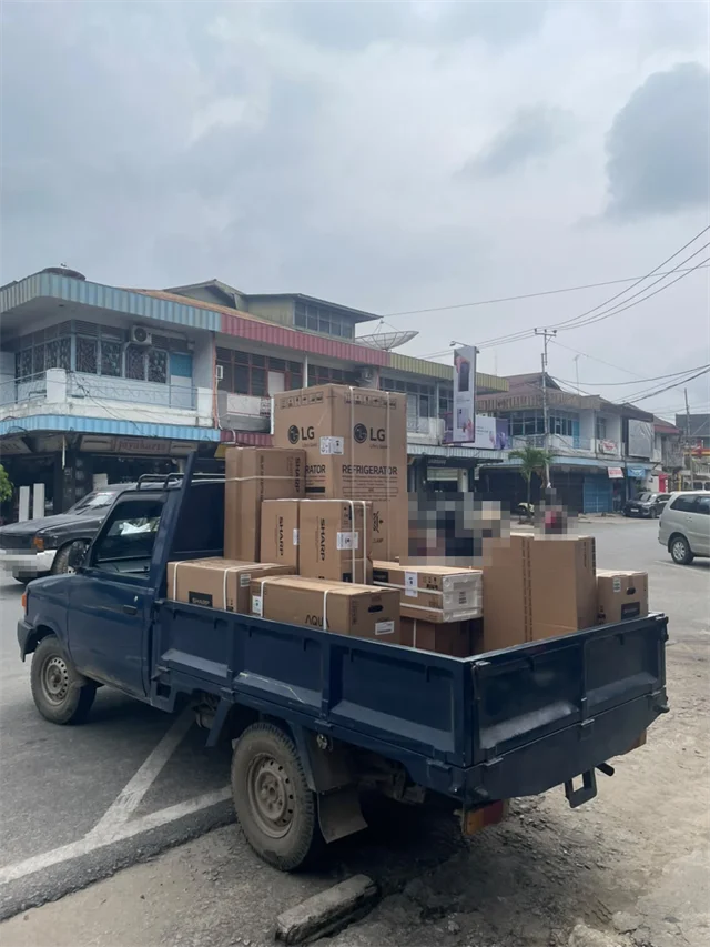 Mobil pick-up berisi dus kulkas LG, dus Sharp, dan dus Aqua di depan toko Hiburan Baru